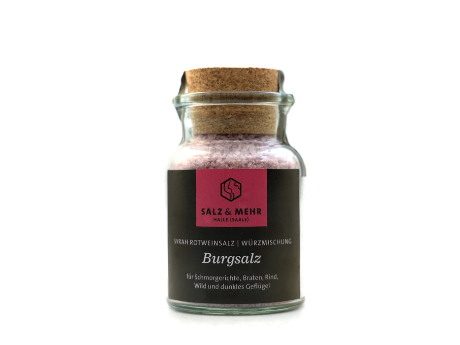 Ein großes Glas mit Korkdeckel und der Aufschrift „Salz & Mehr-Bundle ‚Burgsalz groß mit Salzschaufel‘“ enthält violettes Salz für Schmorgerichte, Rindfleisch, Wild und dunkles Geflügel. Das dunkle Etikett trägt ein rosa quadratisches Logo und wird mit einer Salzschaufel geliefert.