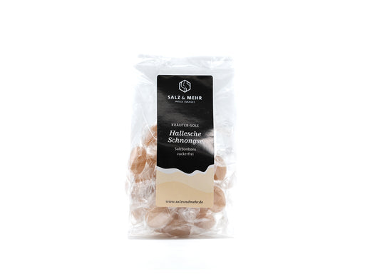 Ein transparenter Beutel mit der Marke Soole eG enthält die veganen, verpackten Halleschen Schnongse – Salzbonbons „Kräuter-Sole“ zuckerfrei. Er ist mit einem hellbraunen Akzent versehen und zeigt die Website am unteren Rand. Das minimalistische Design hebt sowohl Kräuter-Sole- als auch Salzbonbon-Elemente sowie den Produktnamen und die Marke hervor.