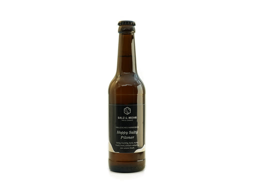 Eine braune Glasbierflasche mit schwarzem Deckel und schwarzem Etikett mit der Aufschrift „Hallesches Hansebier Hoppy Salty Pilsner“ in weißer Schrift steht aufrecht und zentriert vor einem schlichten weißen Hintergrund. Dieses Craft Beer stammt vom Halleschen Brauhaus.