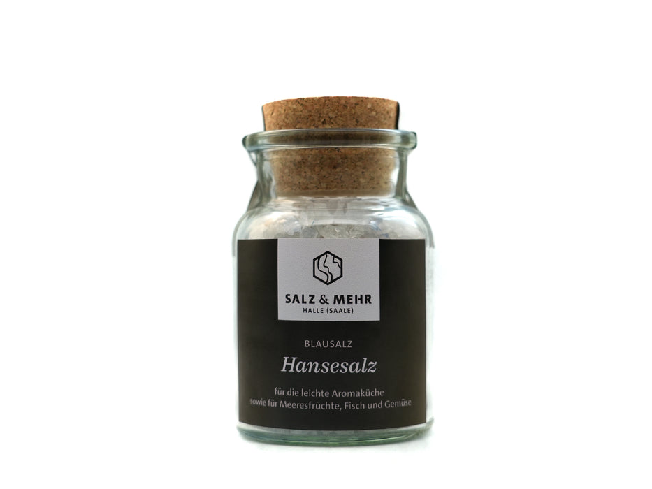 Ein klares Glasgefäß mit Korkdeckel enthält grobes Salz mit der Aufschrift „Salz & Mehr-Bundle Hansesalz groß mit Salzschaufel“ und einem deutschen Text über die Verwendungsmöglichkeiten für Meeresfrüchte, Fisch und Gemüse.