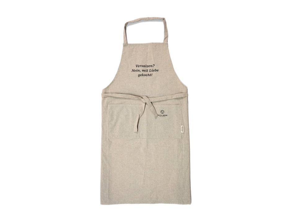 Die beige Kochschürze „Versalzen? Nein, mit Liebe gekocht!“ Aus recyceltem Material hat ein Hals- und Taillenband, zwei große Fronttaschen und sauberen schwarzen Text auf der Vorderseite. Sie wirkt neu und unbenutzt.