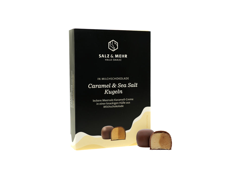Eine Schachtel hallesaale* | Shop Pralinen mit dem eleganten Aufdruck „Kugeln ‚Karamell & Meersalz‘“. Sie enthält gefüllte Halloren Kugeln, von denen eine mit cremiger Milchschokolade gefüllt ist. Die Verpackung ist minimalistisch mit schwarzen und goldenen Akzenten.