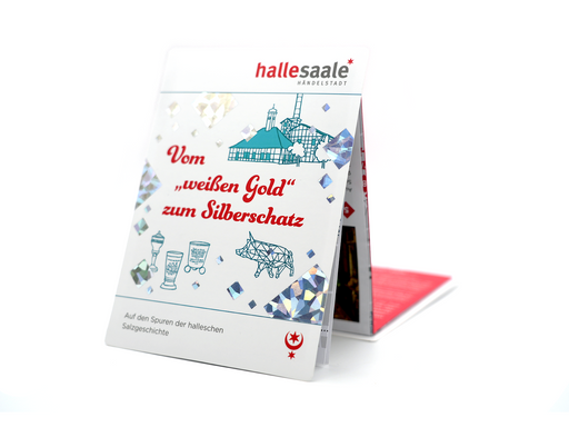 Der gefaltete Kulturstadtplan „Vom weißen Gold zum Silberschatz“ steht aufrecht, auf dem Umschlag ist eine blaue Illustration historischer Gebäude, glänzende Rauten und ein roter Titeltext zu sehen, der die Hallesche Salzgeschichte und das Halloren-Erbe widerspiegelt.