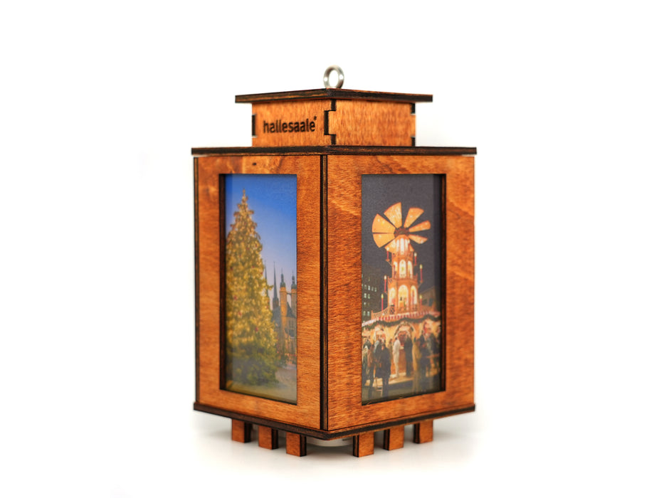 Die Holzlaterne „Halle (Saale)“ ist ein hölzernes, laternenförmiges Ornament mit lasergeschnittenen Kanten, bunten Weihnachtsbaum- und Marktmotiven, einer LED-Lichterkette, einer Aufhängeöse und der Gravur „Hallesaale“ auf der Oberseite. Der Hintergrund ist schlicht weiß.