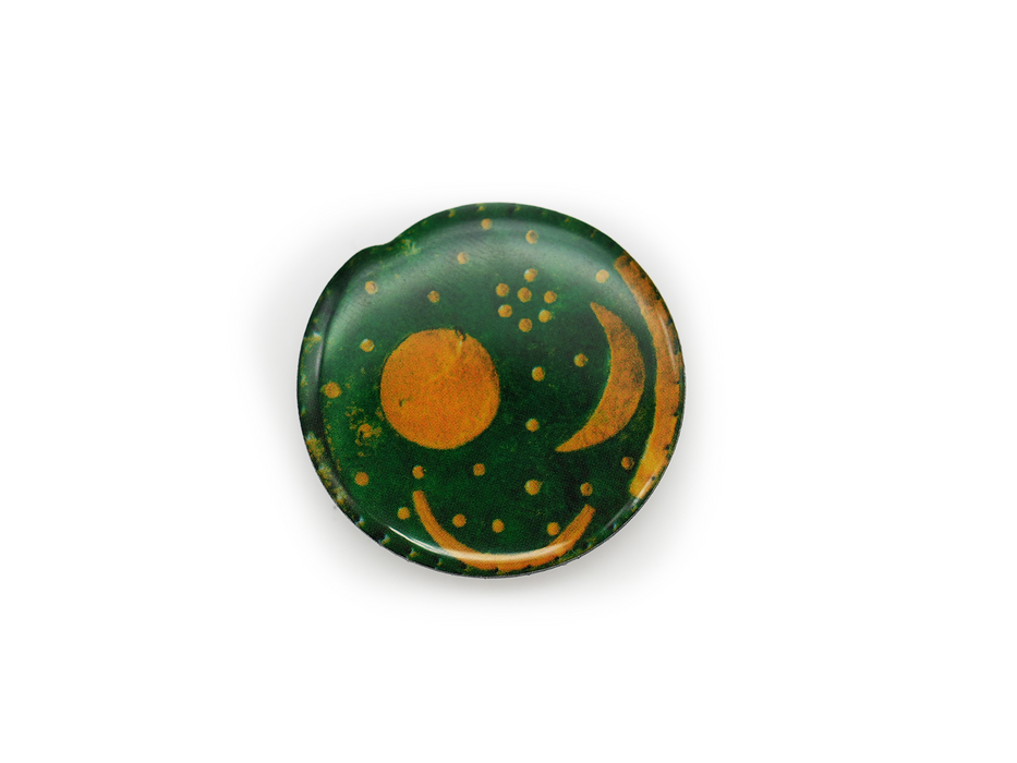 Der Magnet „Himmelsscheibe von Nebra“ zeigt eine runde grüne Scheibe mit goldener Sonne, Halbmond und Sternen – eine Anspielung auf einen antiken Nachthimmel. Sichtbare Abnutzungserscheinungen und Patina unterstreichen den geheimnisvollen und historischen Charme des Magneten.