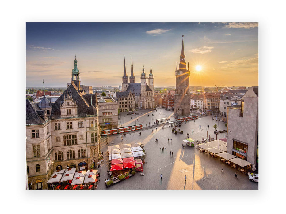 Die Postkarte „Hallescher Marktplatz“ zeigt den belebten Platz bei Sonnenuntergang mit historischen Gebäuden, Kirchtürmen wie der Marktkirche und dem Roten Turm, rot-weißen Vordächern, Straßenbahnen und Menschen in goldenem Licht mit langen Schatten.