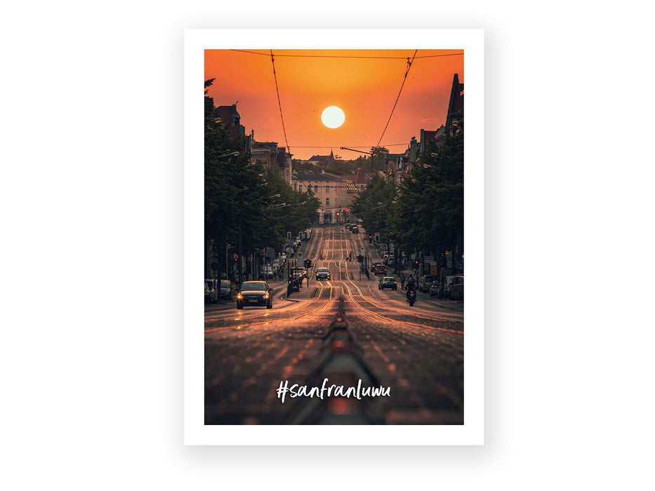 Eine Straße in halle Saale bei Sonnenuntergang, mit Autos und einer Straßenbahn auf hügeligen Gleisen – Bäume und Gebäude säumen diesen malerischen Anblick. Die Postkarte „SanFran LuWu“ fängt eine der Sehenswürdigkeiten der Stadt ein. #sanfranlum steht darunter.