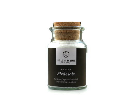 Ein großes Glas mit der Aufschrift „Siedesalz groß“ (99,9 g), gefüllt mit weißem Salz und mit einem Korken verschlossen, trägt ein schwarzes „Salz & Mehr“-Etikett mit dem Hinweis, dass es ohne Jod ist – perfekt für den täglichen Gebrauch. Das Produkt ist vor einem schlichten weißen Hintergrund fotografiert.