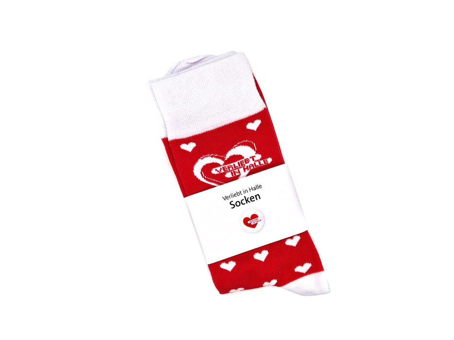 Die Socken „Verliebt in Halle“ sind kuschelige Bio-Baumwollsocken in Rot mit weißen Herzen, gefaltet und im weißen Label mit zwei verschlungenen Herzen und dem Schriftzug „Verliebt in Halle“, produziert in Europa.
