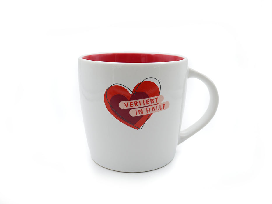 Die Tasse „Verliebt in Halle“ (weiß-rot) ist ein weißer Becher mit roter Innenseite. Auf der Vorderseite ist vor einem schlichten weißen Hintergrund ein kräftiges rotes Herz und „VERLIEBT IN HALLE“ in weißen Buchstaben abgebildet.