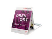 Der gefaltete Kulturstadtplan „Drehort Halle (Saale)“ steht auf weißem Untergrund. Sein violetter Einband mit weißer Schrift zeigt eine Stadtansicht, hebt Filmproduktionen hervor, präsentiert Drehorte und zeigt oben das Logo „halle saale“ mit rotem Stern.