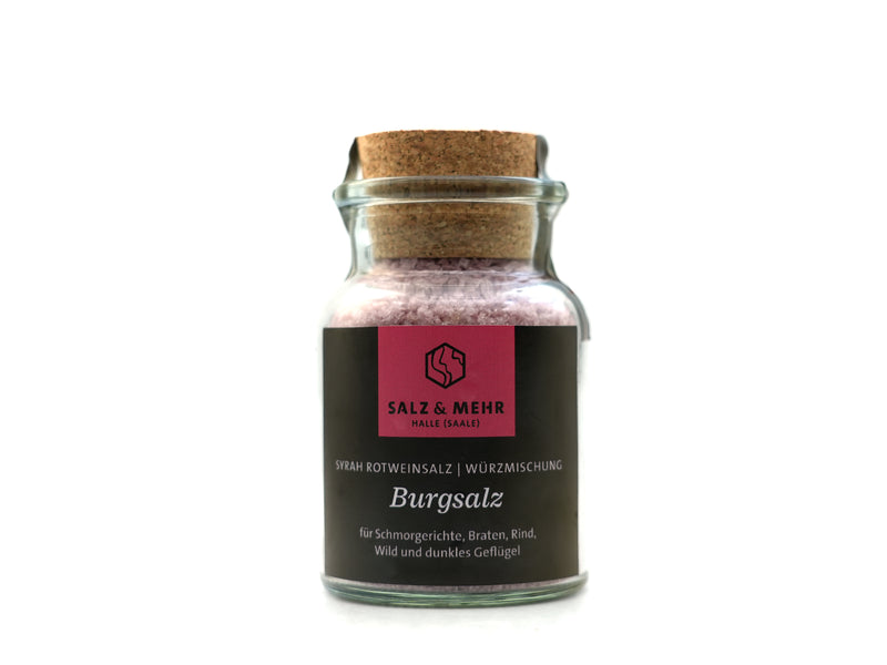 Ein großes Glas mit Korkdeckel und der Aufschrift „Salz & Mehr-Bundle ‚Burgsalz groß mit Salzschaufel‘“ enthält violettes Salz für Schmorgerichte, Rindfleisch, Wild und dunkles Geflügel. Das dunkle Etikett trägt ein rosa quadratisches Logo und wird mit einer Salzschaufel geliefert.