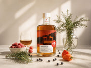 Flasche Gin Luwu Reserve (im Sherryfass gereift) mit bernsteinfarbener Spirituose und Straßenbahn-Etikett, dekoriert mit Himbeeren, Habanero-Chilis und Wacholderbeeren.