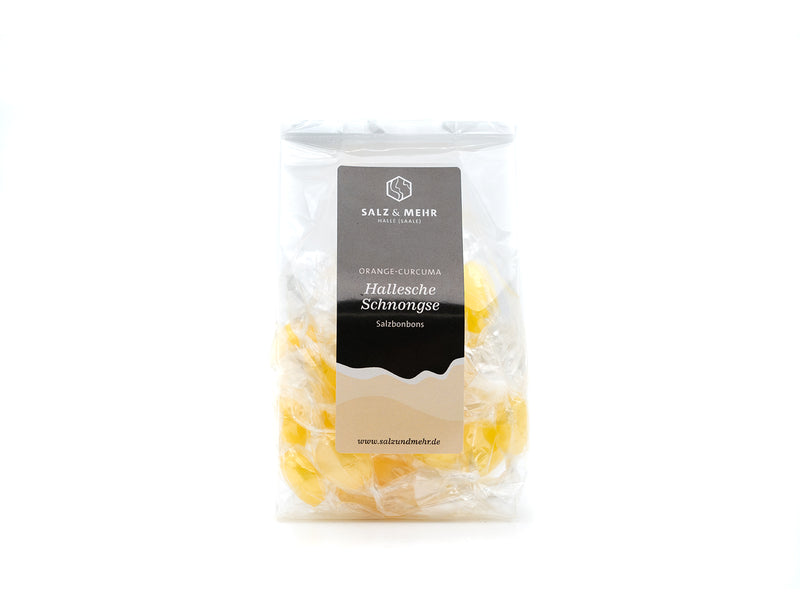 In einer durchsichtigen Plastiktüte sind einzeln verpackte gelbe Bonbons mit Orangen-Kurkuma-Geschmack zu sehen. Auf dem Etikett steht „Soole eG, Hallesche Schomgse Salzbonbons“, und die versiegelte Verpackung ist auf weißem Grund angebracht.