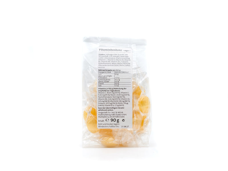 Eine transparente Plastiktüte mit Halleschen Schnongse – Salzbonbons „Vitamin-Sole“ zuckerfrei (90 g) ist von hinten abgebildet. Das weiße Etikett listet Zutaten, Nährwerte und Gewicht auf. Die gelben, veganen Bonbons sind einzeln in transparenter Folie verpackt.