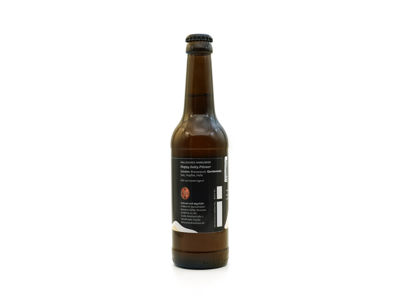Eine ungeöffnete Braunglasflasche des Halleschen Hansebier „Hoppy Salty Pilsner“ steht aufrecht auf weißem Untergrund, zentral platziert. Das schwarze Etikett mit weißem Text und einem roten Kreis zeigt Produktdetails in deutscher Sprache.