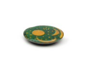 Der Magnet „Himmelsscheibe von Nebra“ besticht durch sein rundes, flaches Design mit dunkelgrüner Oberfläche und goldenen Motiven von Sonne, Halbmond und Sternen – eine Reminiszenz an die Himmelsscheibe. Präsentiert auf schlichtem, weißem Hintergrund wirken die Ränder sanft verschwommen.