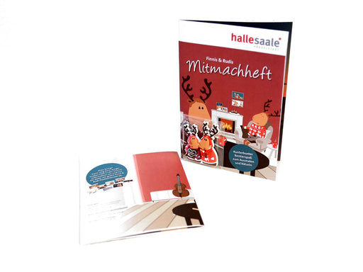 Abgebildet sind zwei Hefte: das stehende Mitmachheft „Finni & Rudi“ inkl. Magnet, das Comic-Rentiere in einem festlichen Wohnzimmer zeigt, und ein offenes, flach liegendes Heft mit illustriertem, weihnachtlichem Innenteil.