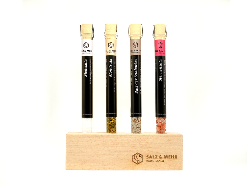 Der Reagenzglashalter von hallesaale* | Shop enthält Reagenzgläser mit Korkstopfen, die weiße, grüne, beige und rosa Salze enthalten. Jedes Röhrchen ist beschriftet und wird aufrecht in einem hellen Holzhalter mit den Gravuren „Salz & Mehr“ und „Halle (Saale)“ auf schlichtem weißem Hintergrund aufbewahrt.