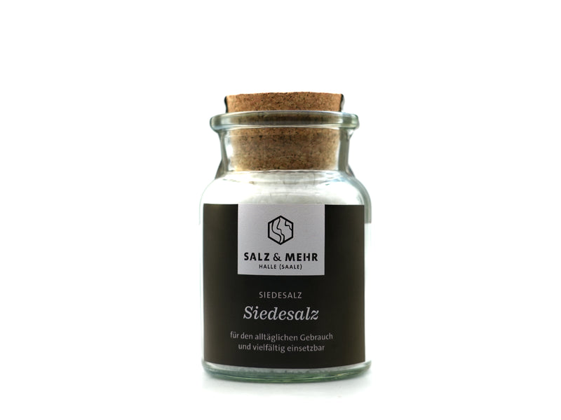 Ein großes Glas mit der Aufschrift „Siedesalz groß“ (99,9 g), gefüllt mit weißem Salz und mit einem Korken verschlossen, trägt ein schwarzes „Salz & Mehr“-Etikett mit dem Hinweis, dass es ohne Jod ist – perfekt für den täglichen Gebrauch. Das Produkt ist vor einem schlichten weißen Hintergrund fotografiert.