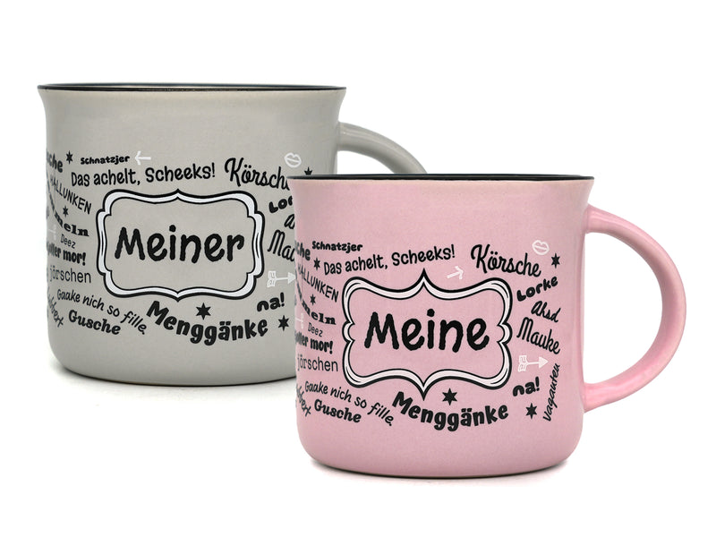 Produktfoto mit zwei Keramiktassen im Emaille-Becher-Stil vor weißem Hintergrund: Eine graue Tasse mit der Aufschrift „Meiner“ links hinten und eine rosa Tasse mit dem Schriftzug „Meine“ rechts im Vordergrund, jeweils umgeben von halleschen Dialekt-Wörtern.