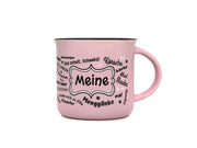 Rosa Keramiktasse in klassischer Emaille-Becher-Form mit schwarzem Innenrand. Auf der Frontseite befindet sich der Schriftzug „Meine“ in einem geschwungenen Rahmen, umgeben von halleschen Mundart-Begriffen wie „Körsche“, „Mauke“ und „Menggänke“.