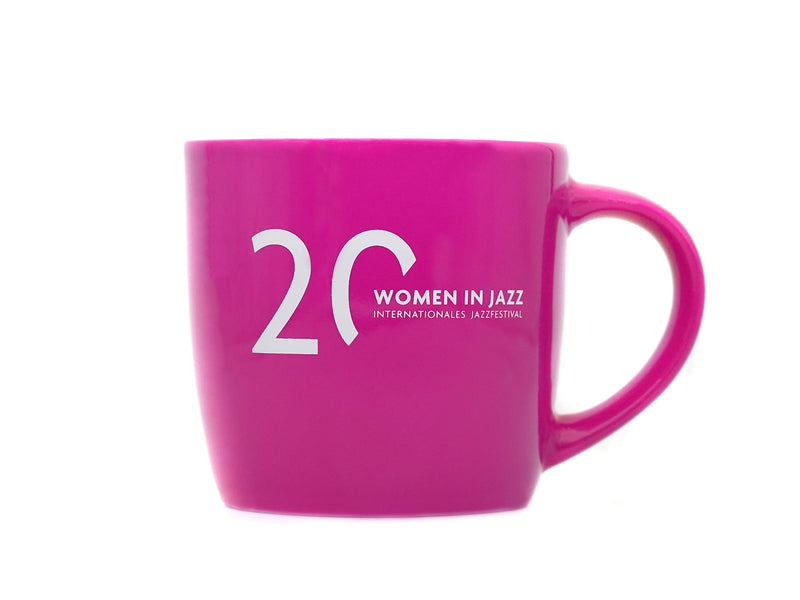 Die Tasse „Women in Jazz“ ist eine leuchtend rosa Keramiktasse mit großem Henkel. Der weiße Schriftzug „20 WOMEN IN JAZZ INTERNATIONALES JAZZFESTIVAL“ feiert das 20-jährige Jubiläum des Festivals. Der Hintergrund ist schlicht weiß.