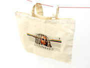 Der Leinenbeutel „Graffiti-Händel“ ist ein beigefarbener Fairtrade-Baumwollbeutel, der an einer roten Schnur auf weißem Hintergrund hängt. Er zeigt den Komponisten Händel mit Sonnenbrille und einem Regenbogenstrahl im Haar. Darunter ist „HANDEL“ aufgedruckt.